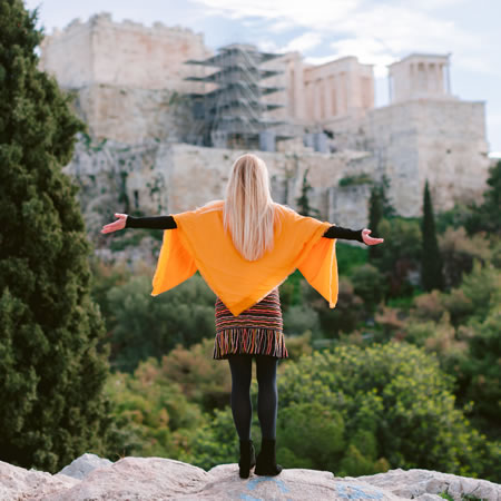 Melanie Marten with back turned and arms outstretched towards the ancient Greek architecture
