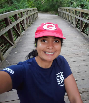 Nidhi Gupta taking a selfie on a bridge wearing a red hat