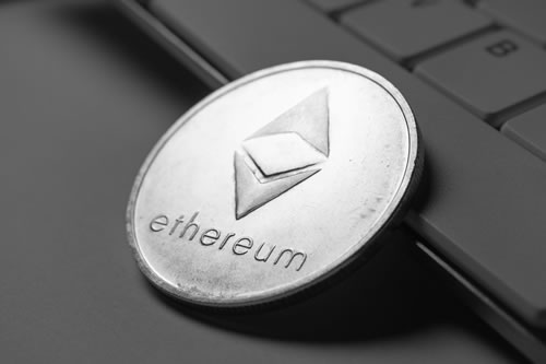 a silver Ethereum coin laying up against a keyboard