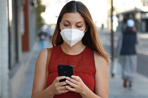 girl with mask looking at cellphone and walking