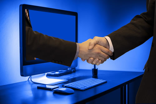 Two men handshaking through a PC monitor