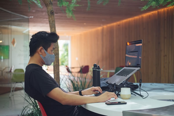 man with mask working remote on his laptop