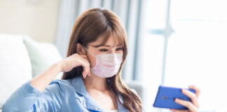 Technology Addiction Leading to an Unhealthy Covid-19 Response woman wearing mask sitting on couch reading cell phone