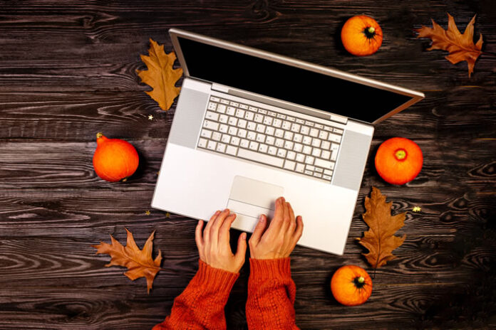 top view of girl typing on laptop with autumn leaves and pumpkins around