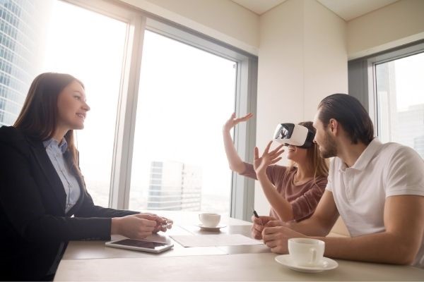 3 people sitting at a table while one person is viewing a presentation with vr goggles