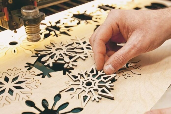man cutting out snowflakes on poster board with laser cutter