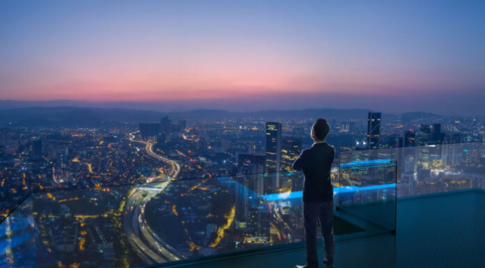 Tips For Leaders on How to Thrive During Trying Times – Like COVID19 business man looking out over the city from the top of a skyscraper at dusk