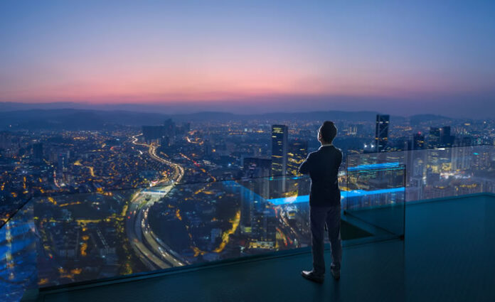 business man looking out over the city from the top of a skyscraper at dusk