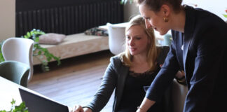 two women discussing business success at a desk with a laptop