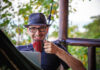 man smiling as he sips his coffee working remotely from his front porch