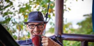 man smiling as he sips his coffee working remotely from his front porch