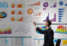 business man pointing to large electronic dashboard with colorful graphs and charts