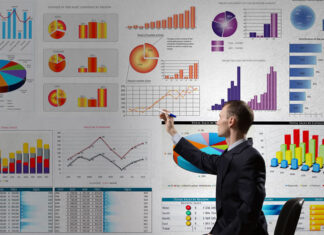 business man pointing to large electronic dashboard with colorful graphs and charts