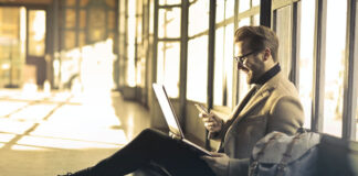 The Technology That Will Power the Hybrid Work Model man sitting on the floor with his laptop and phone as he works remote