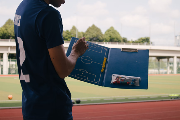 soccer coach displaying play field on notebook to his team