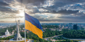 The War Between Russia and Ukraine is Affecting Staff Augmentation Ukraine flag flying in Kyiv over a city of businesses and staffing