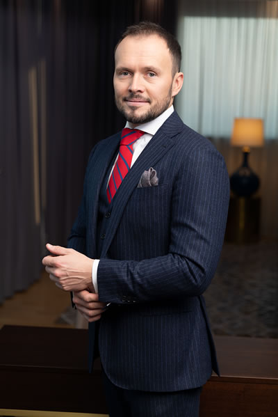 Bartosz Skwarczek standing in blue suite and red tie