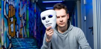 The Invisible Threat of Deepfake Phishing hacker holding up a mask by laptop representing deepfake phishing