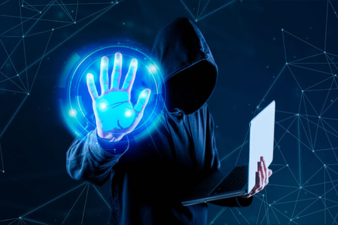 hacker with laptop holding up hand to launch cyber threats