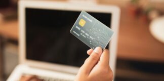 Corporate Cards: An Effective Tool for Financial Management woman holding up one of her corporate cards to make a purchase on her computer