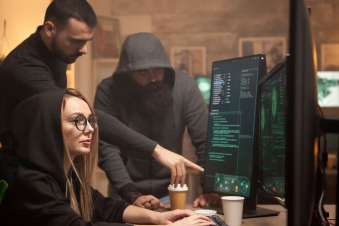 Three hackers around a monitor performing Ddos attacks.