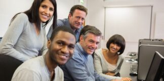 Staff Augmentation vs Managed Services: Making the Right Choice office with staff augmentation to help with tech, shown with 5 people around a computer