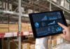 AI in Inventory Optimization: Meeting Consumer Demand Accurately AI in inventory optimization, shown with a hand holding a tablet in a warehouse