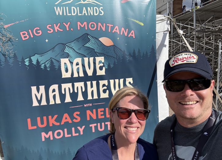 Christopher Sprague smiling with his wife and a Montana sign in the background.